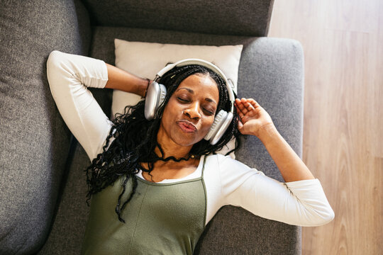 Serene black woman enjoying music on sofa at home