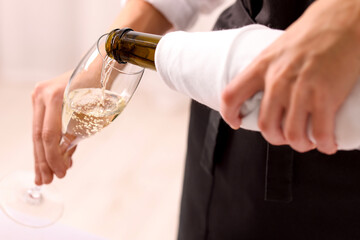 Waiter pouring champagne into glass indoors, closeup