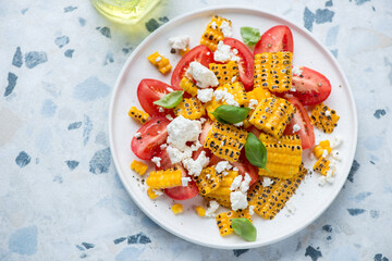 Plate with tomato, grilled corn and cheese salad, horizontal shot on a white and blue granite...