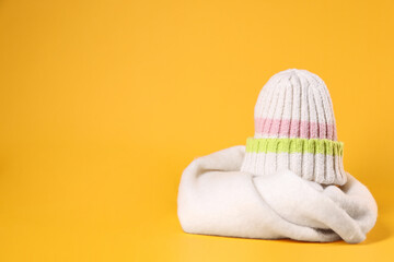 Stylish knitted hat and warm scarf on yellow background, space for text