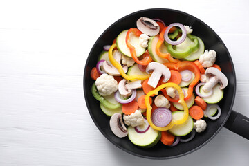 Frying pan with mix of vegetables and mushrooms on white wooden table, top view. Space for text