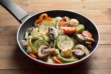 Different vegetables and mushrooms in frying pan on wooden table, closeup