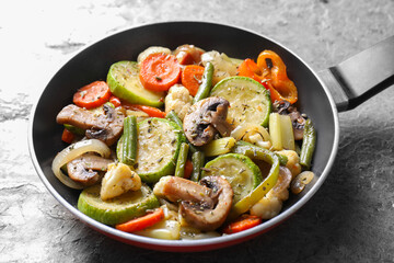 Different vegetables and mushrooms in frying pan on grey textured table, closeup