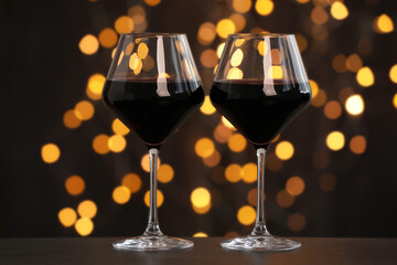 Tasty red wine in glasses on table against dark background with blurred lights, bokeh effect
