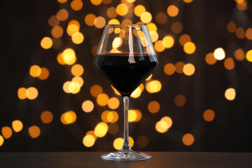 Tasty red wine in glass on table against dark background with blurred lights, bokeh effect