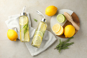 Lemon water with lime in bottles, rosemary, fresh fruits and squeezer on grey table, flat lay
