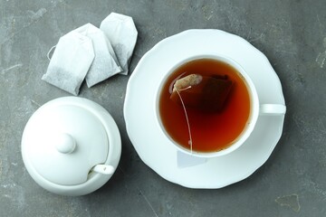 Tea bags and cup with hot drink on gray textured table, flat lay
