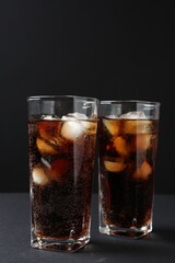 Refreshing cola with ice cubes in glasses on black table, closeup