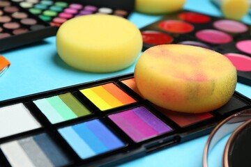 Bright face paints and sponges on light blue background, closeup