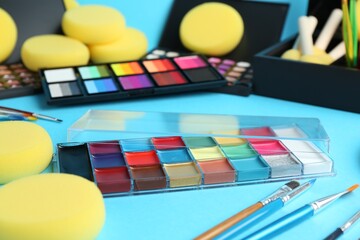 Bright face paints, brushes and sponges on light blue background, closeup