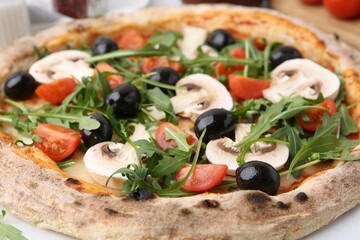 Tasty pizza with cherry tomatoes, black olives, mushrooms and arugula on white table, closeup