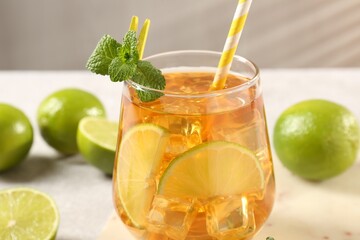 Fototapeta premium Refreshing iced tea with slices of lime, mint and drinking straw in glass on light table, closeup