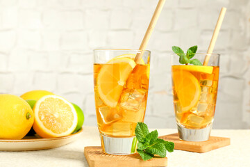 Refreshing iced tea with drinking straws, mint and lemon on light textured table against grey background, closeup