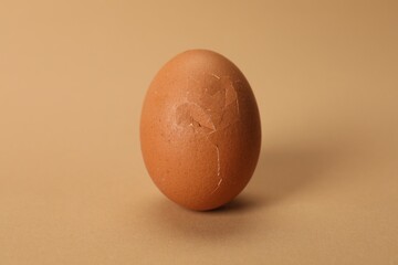 One egg with cracked shell on beige background, closeup