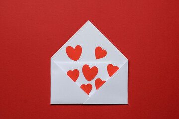 Valentine's Day. Envelope with many paper hearts on red background, top view