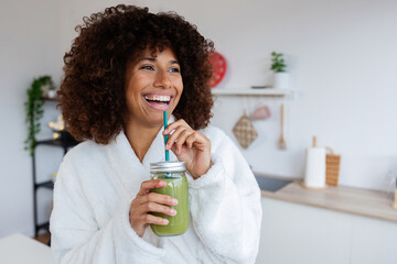 Portrait of mixed race beautiful young woman drinking healthy green juice in the morning standing...