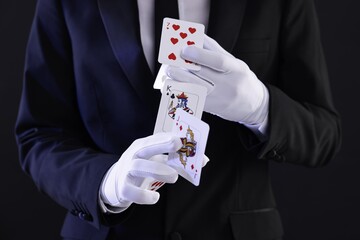 Illusionist showing trick with playing cards on black background, closeup