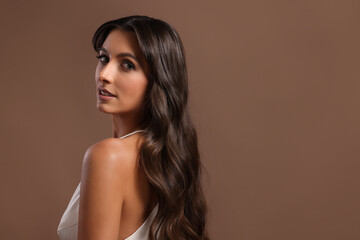 Hair styling. Portrait of beautiful woman with wavy long hair on brown background, space for text