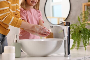 Mother and daughter washing their hands above sink indoors, closeup