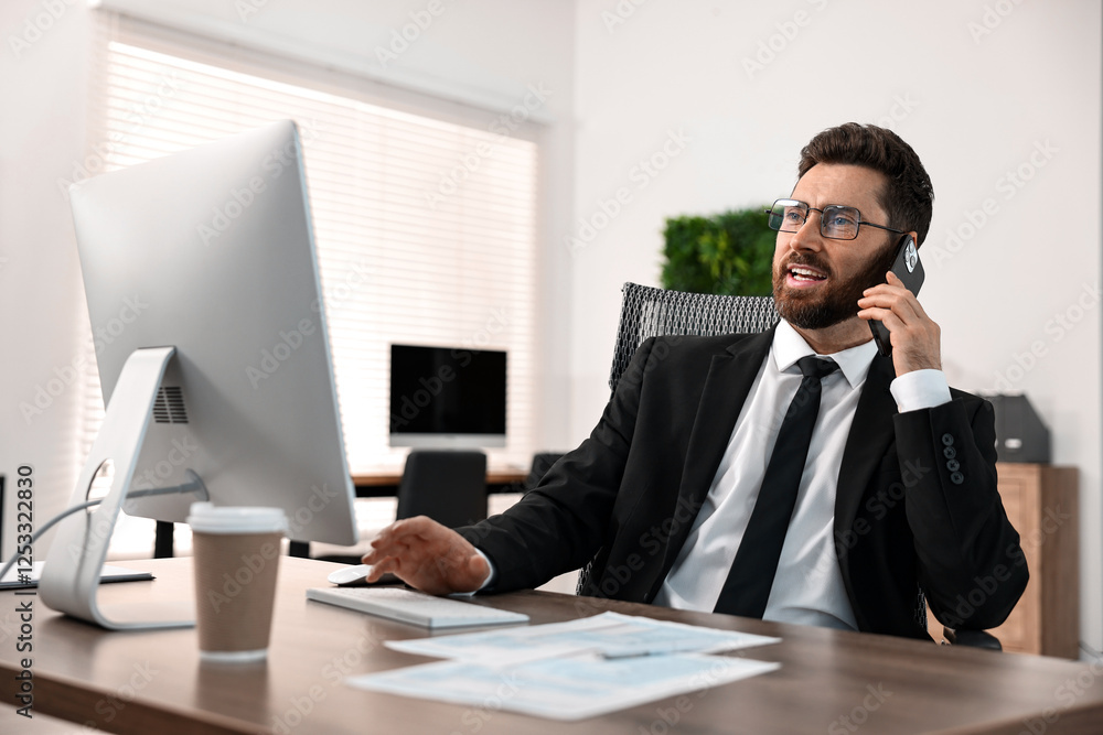 Poster man talking on smartphone while working at table in office