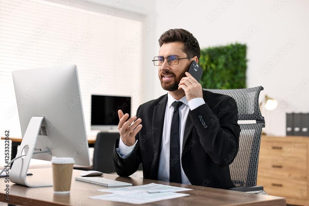 Poster man talking on smartphone while working at table in office