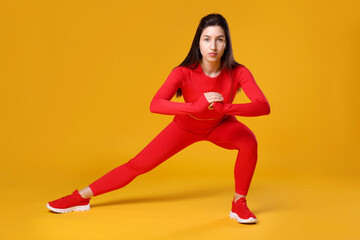 Woman in sportswear exercising on orange background