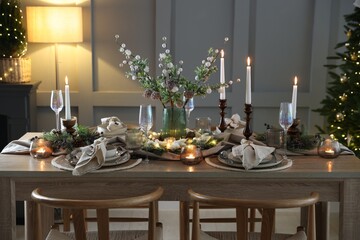 Christmas table setting with stylish dishware, glasses and burning candles in festive decorated room
