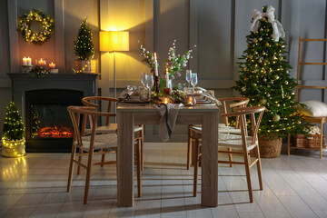 Christmas table setting with stylish dishware, glasses and burning candles in festive decorated room