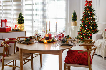 Christmas table setting with stylish dishware, glasses and burning candles in festive decorated room