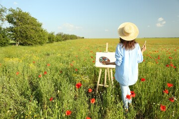 Woman painting on easel in beautiful poppy field, back view