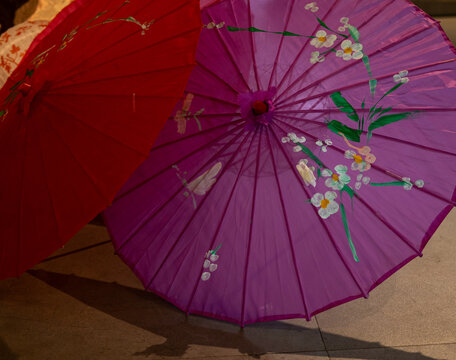 Close-up of vibrant Chinese hand-painted umbrellas.  Detailed floral designs in pink and white adorn the colorful canopies, showcasing traditional craftsmanship and artistry.
