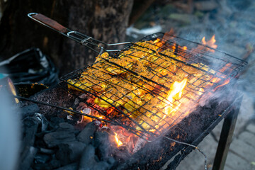 Man grilling chicken over charcoal at a food stall (warung), delicious ayam bakar with smoke. Mouth-watering Indonesian cuisine.