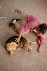 Smiling woman petting a relaxed German Shepherd lying on carpet floor. Canine seems comfortable and at ease while being gently stroked by its owner