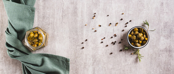 Marinated capers in a bowl, rosemary and peppercorns on the table top view web banner