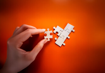 A hand carefully places a wooden jigsaw puzzle piece to complete a small section on a vibrant orange surface, symbolizing problem-solving and connection.