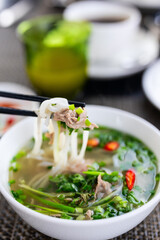 Chopsticks lifting noodles from beef pho