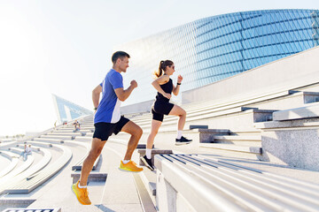 Two individuals exercise by running up outdoor stairs in a modern urban setting during daylight hours