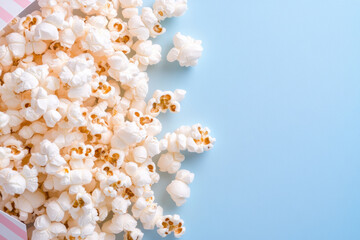 Overflowing popcorn spilling from colorful box onto bright blue background snack concept