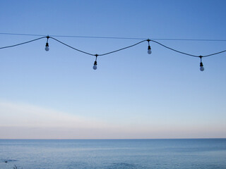Garland with lights by the sea against the background of a blue clear sky. Concept of rest, trip, relaxation, vacation