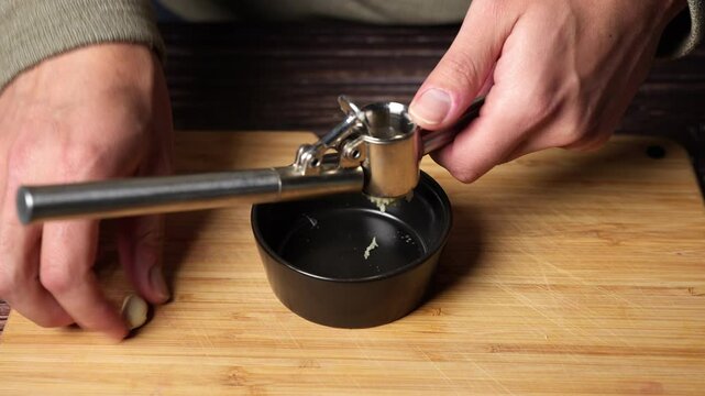 Close-up of chef's hands squeezing a garlic press over a black bowl, crushed garlic falling in slow motion