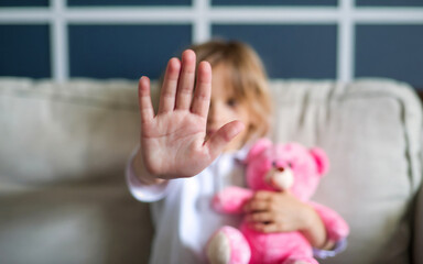 An afraid, sad little girl with stop gesture, at home. Rejection of domestic violence home, child abuse, discrimination, bullying concept.