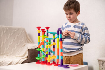 A 5-year-old boy plays with a multi-colored construction set, a labyrinth for balls. Development of logic and fine motor skills in preschool children. Independent play