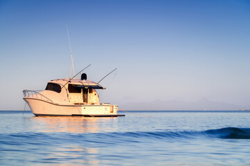 Fototapeta premium Yacht moored on the beach. Morning light illuminating a boat in the sea. Paradise coast.