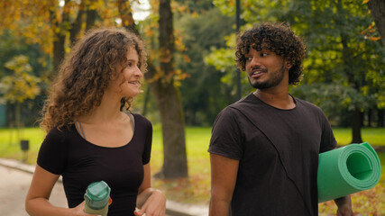 Happy carefree love girlfriend boyfriend multiracial couple friends talking fitness break strolling together cheerful Caucasian woman Indian man walking to yoga class workout sport outdoors in city