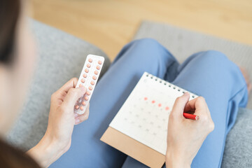 A young female holding birth control pills and a period schedule on the calendar plans to take a pill to control birth.