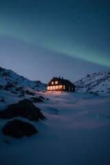 Obraz premium Illuminated cabin in snowy mountains under aurora borealis. Possible use Stock photo for travel, nature, winter, or tourism