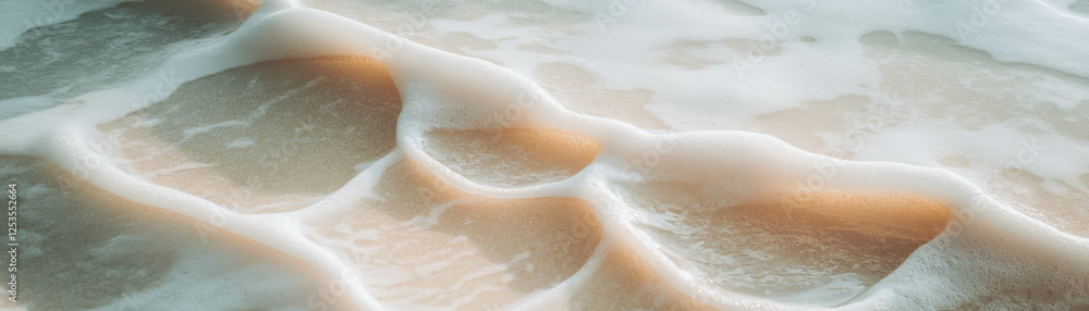 Poster waves recede from shore, revealing intricate wet sand patterns at dawn
