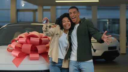 Happy smiling couple African American family woman man new car owners buyers showing keys at camera...
