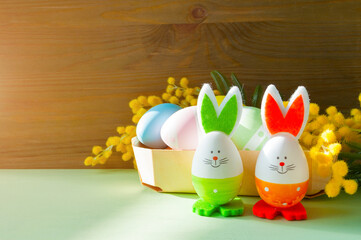 Easter background with cute Easter bunnies and Easter eggs in the nest near the mimosa flowers, copy space for festive Easter text