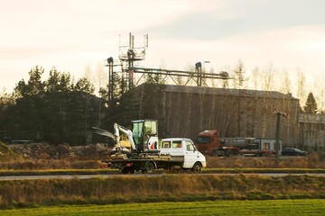 Fototapeta premium Yellow truck transporting excavator on construction site road